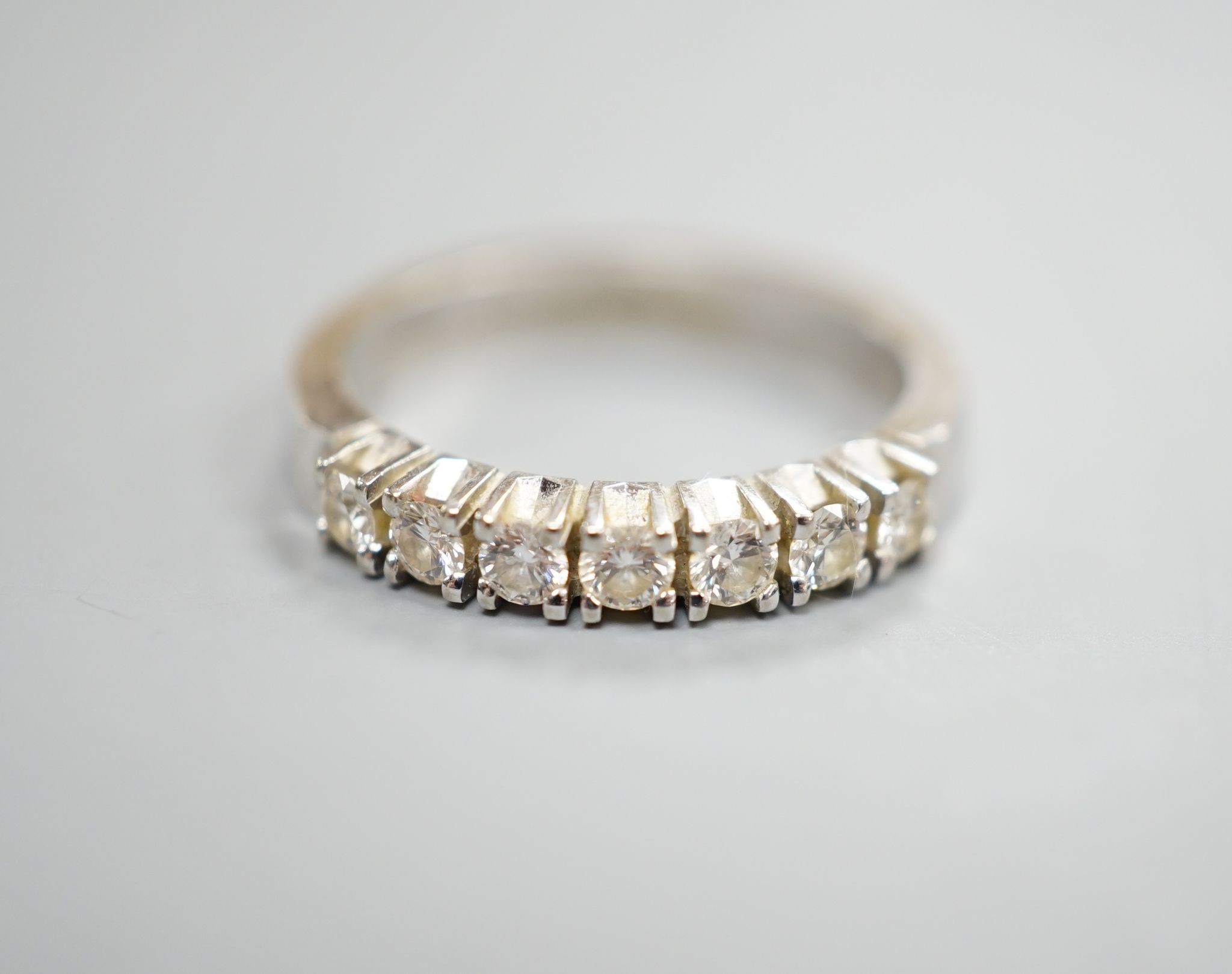 A modern 18k white metal and seven stone diamond set half eternity ring, size M, gross weight 4.4. grams.